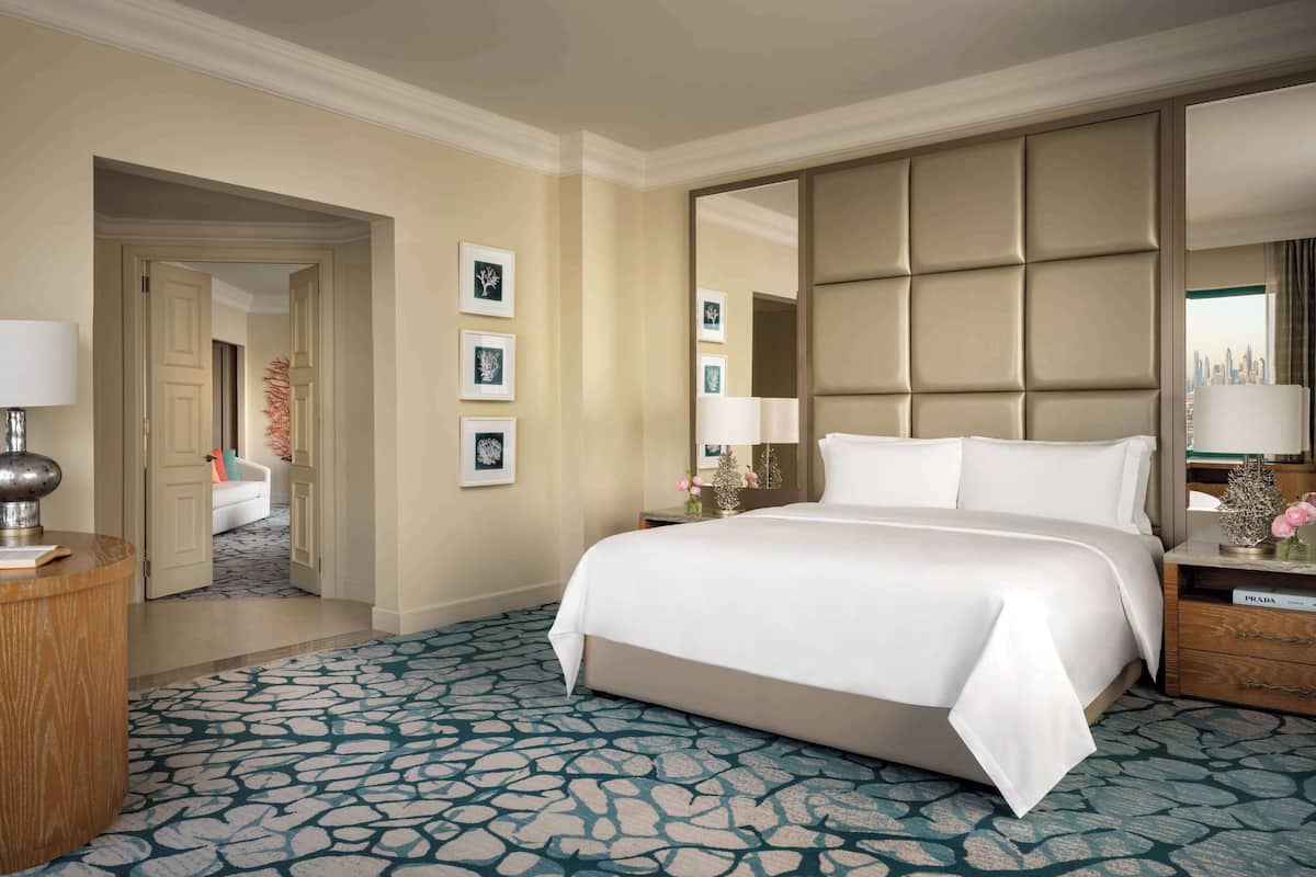 A hotel room with a large bed, a nightstand, a mirror, and a view of a cityscape.