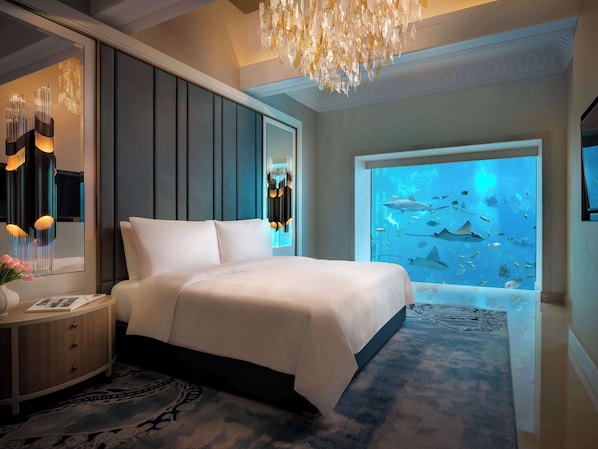 A bedroom with a large bed, a nightstand, a mirror, a chandelier, and an aquarium wall.
