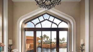 A spacious room with a large arched window, a modern chandelier, a dining area with a marble table, and a seating area with a sofa and armchairs.