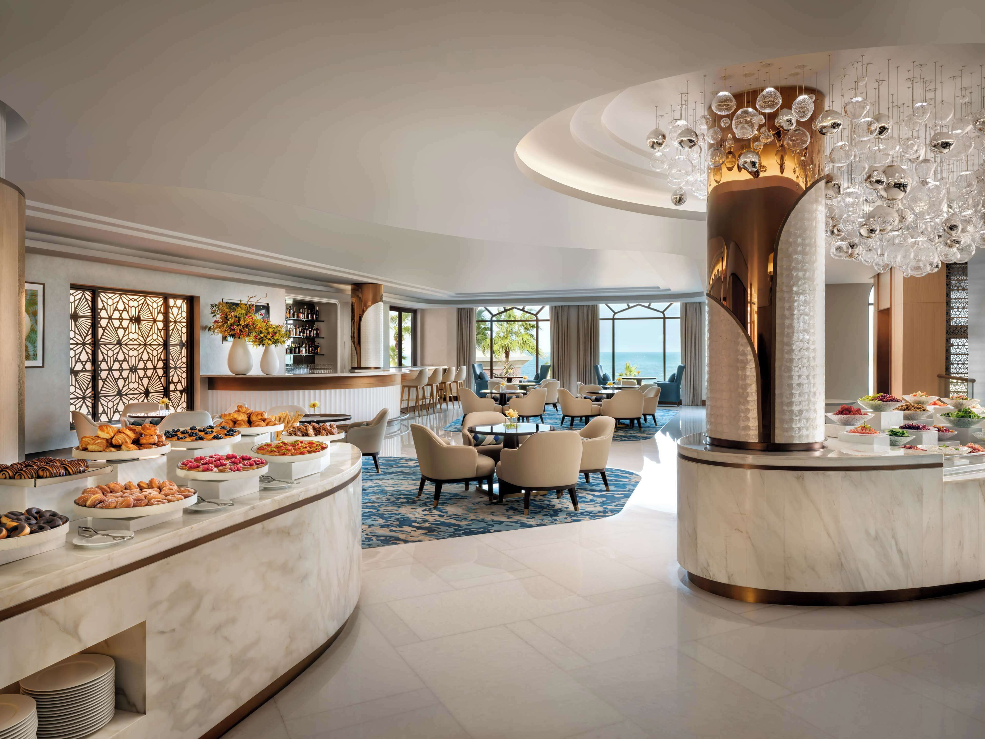 A luxurious hotel lobby with a marble reception desk, a bar area, and a seating arrangement with a view of the ocean.