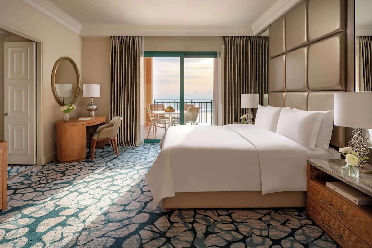 A hotel room with a bed, desk, chair, and a view of the outdoors.