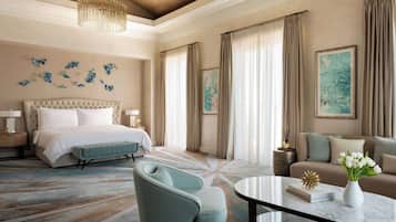 A spacious hotel room with a large bed, a sitting area with a sofa and armchairs, a round coffee table, and a chandelier.