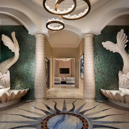 A hallway with a central column, decorative fish sculptures, a patterned floor, and a chandelier.