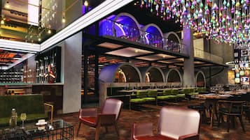 A modern restaurant with a bar area, multiple seating options including booths and tables, and a ceiling adorned with hanging light fixtures.