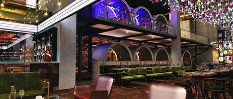 A modern restaurant with a bar area, multiple seating options including booths and tables, and a ceiling adorned with hanging light fixtures.