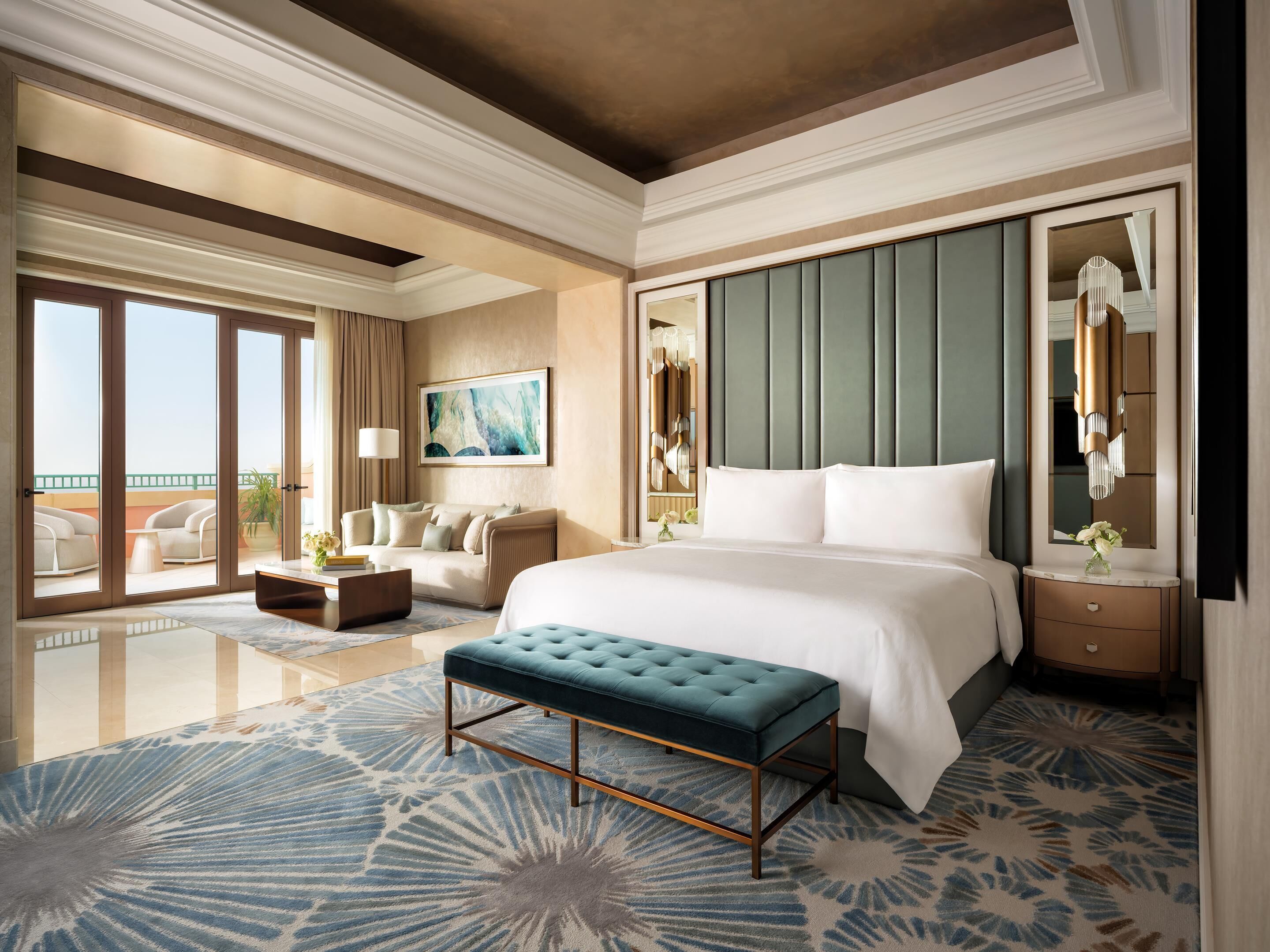 A spacious hotel room with a large bed, a seating area with a sofa and armchairs, a large window with a view, and a decorative mirror.