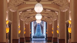 A grand hallway with ornate columns, a central chandelier, and a Christmas tree.