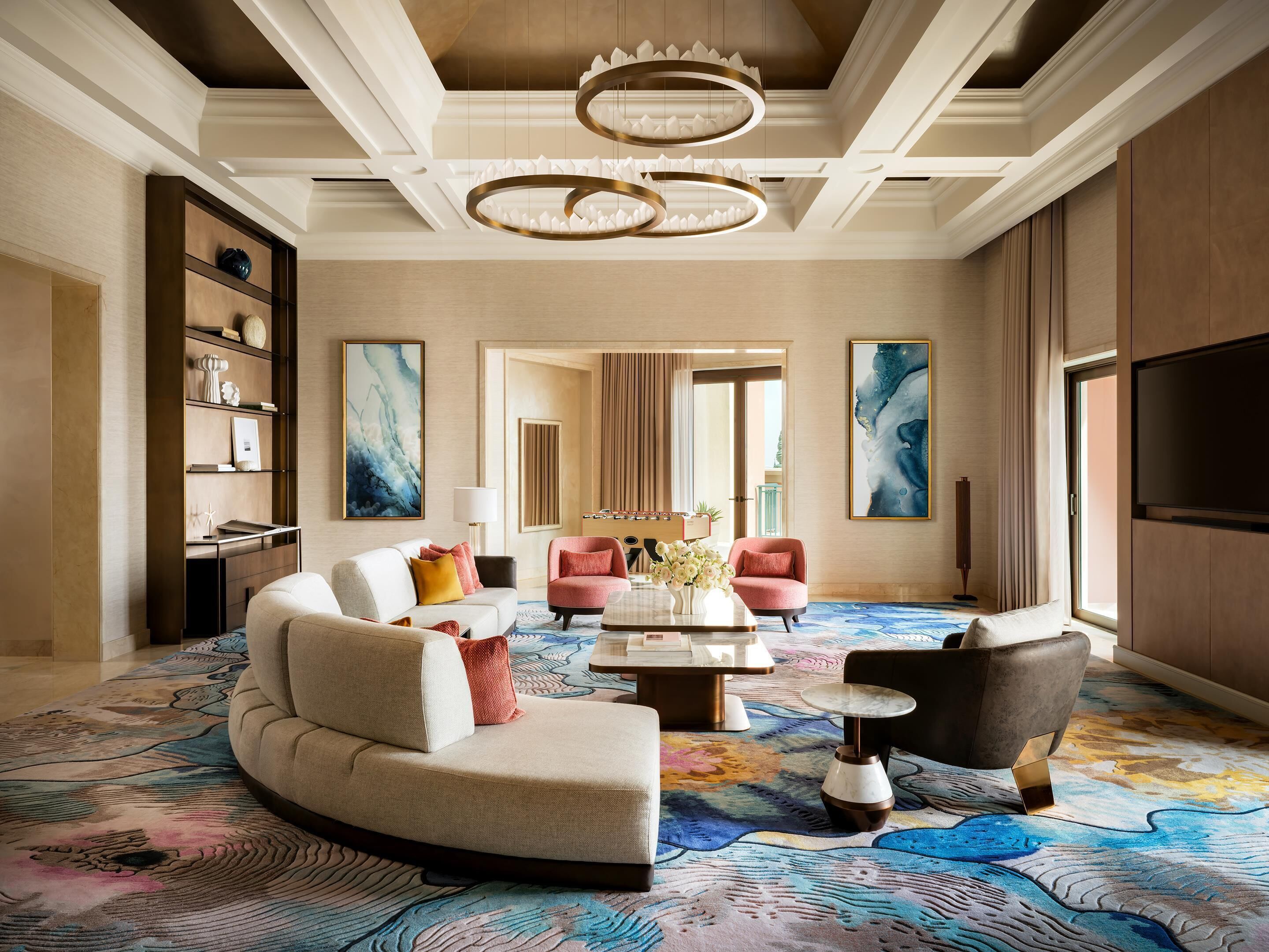 A spacious living room with a curved sofa, two armchairs, a coffee table, and a chandelier.