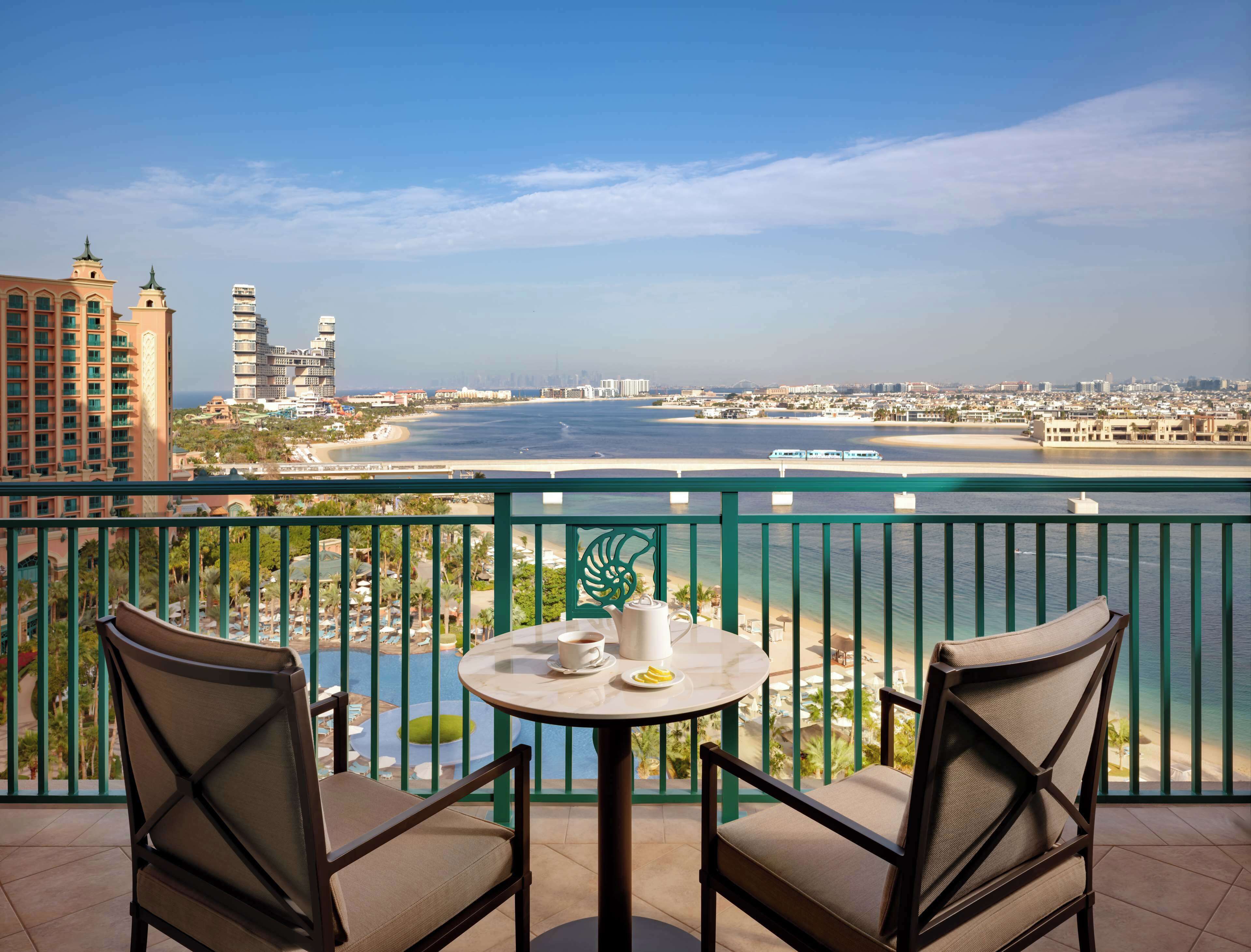 Balcón con dos sillas y una mesa, con vistas a la playa y al paisaje urbano.