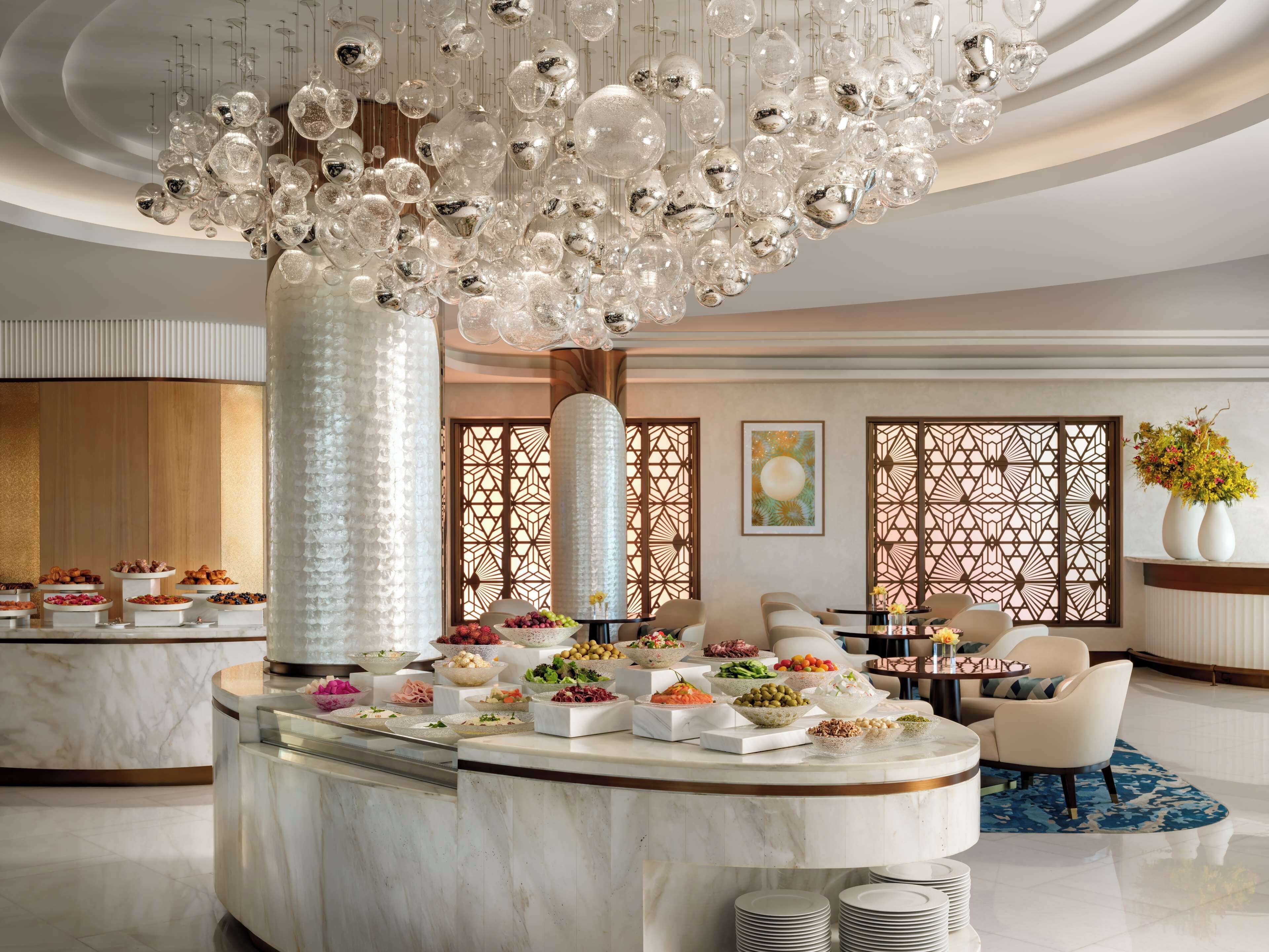 A luxurious hotel lobby with a marble reception desk, a decorative chandelier, and a seating area with sofas.