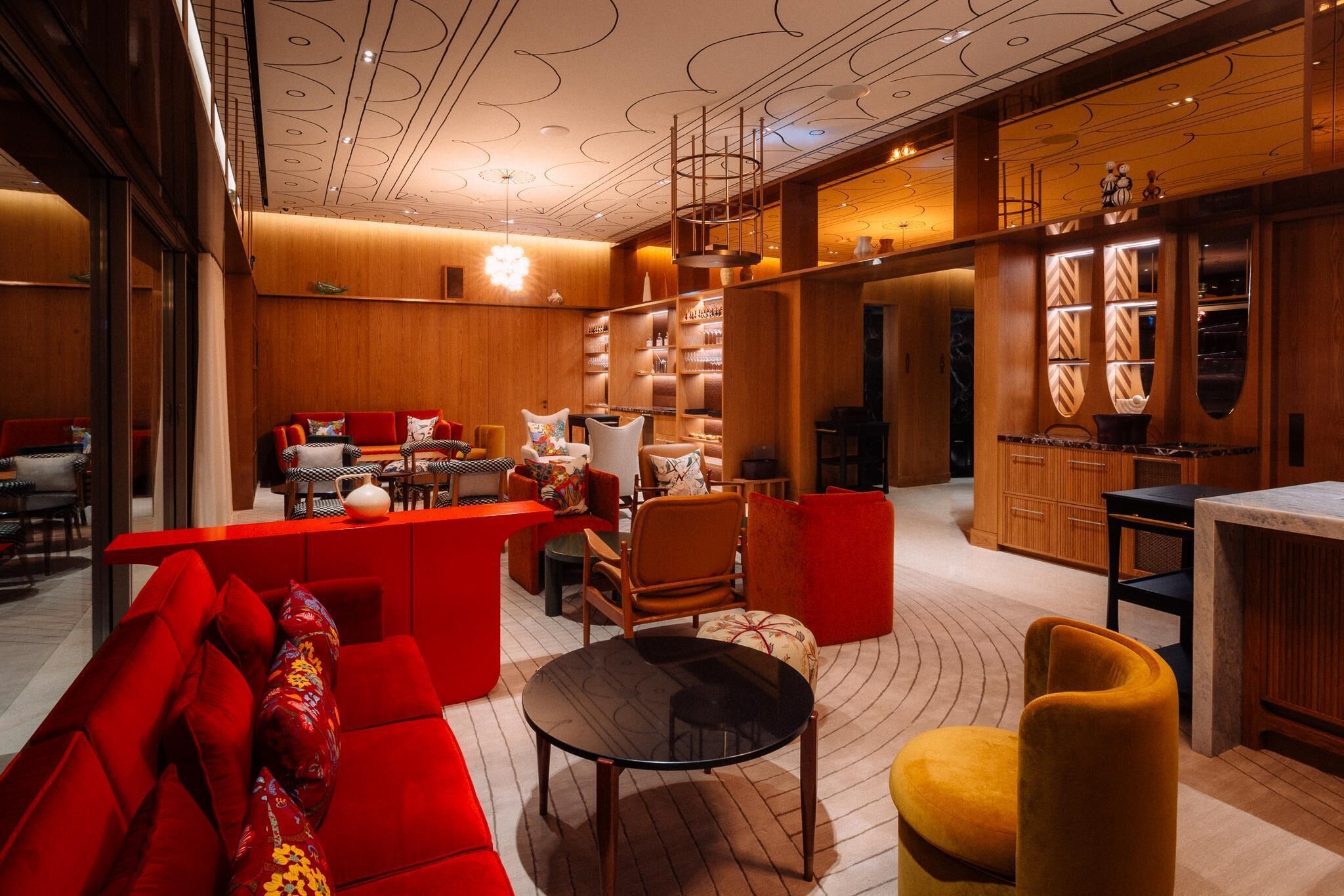 A modern interior with a red sofa, yellow ottoman, and a black table. There are wooden cabinets and a marble countertop.