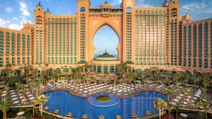 A large hotel with a central pool, multiple balconies, and a distinctive archway.