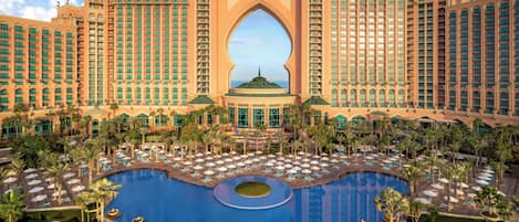 A large hotel with a central pool, multiple balconies, and a distinctive archway.