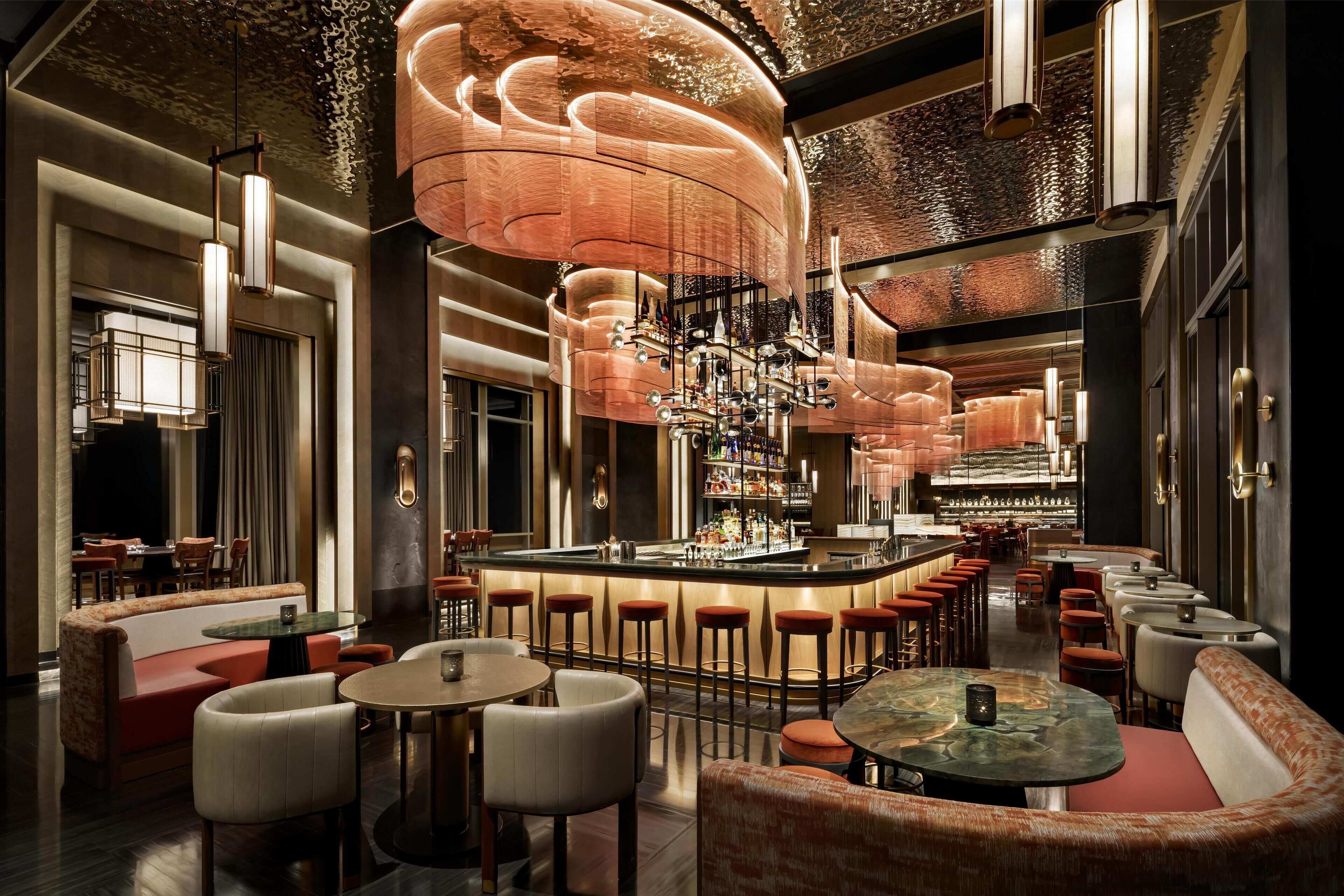 A bar area with high stools, a bar counter, and a seating area with round tables and cushioned chairs.