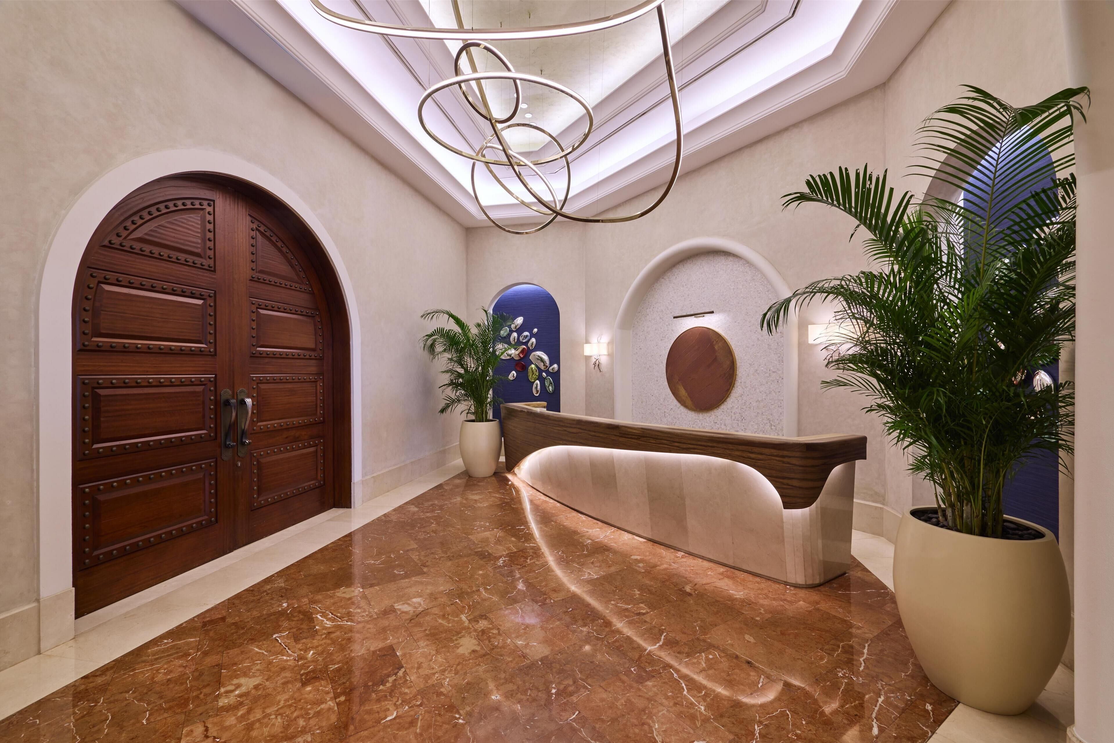 A lobby with a marble floor, a reception desk, a large wooden door, and a potted plant.