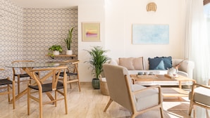 A modern living room with a glass dining table, wooden chairs, a sofa, and a coffee table. There are potted plants and artwork on the walls. - Puerta Catedral Apartments (Seville)