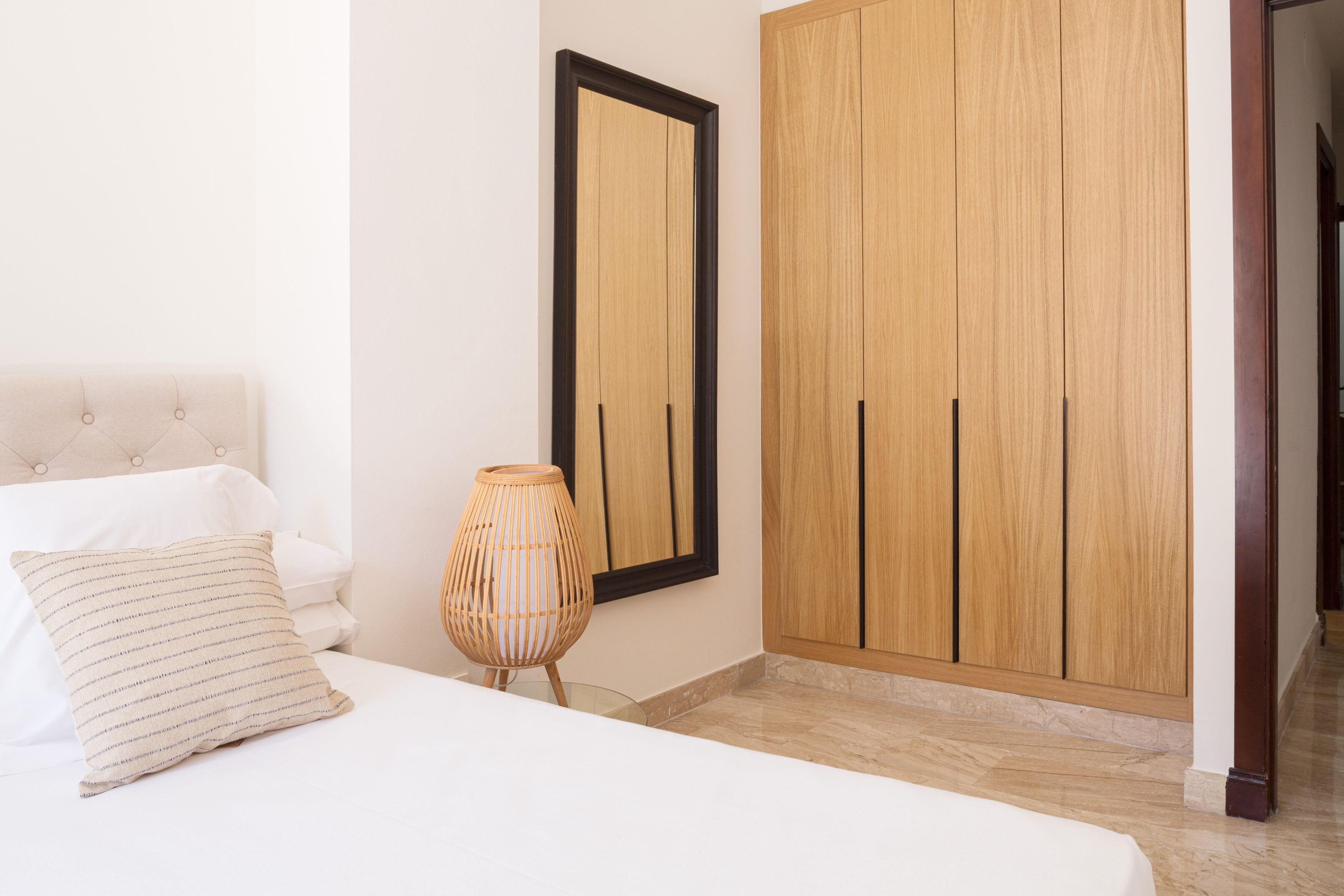 A bedroom with a bed, a bedside lamp, a wardrobe, and a mirror on the wall.
