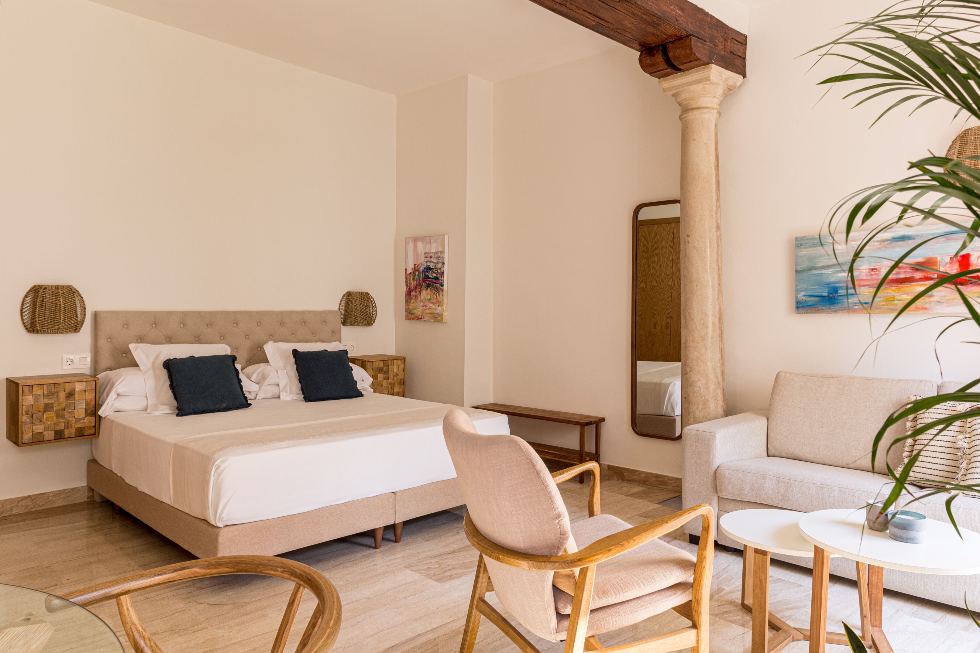 A hotel room with a bed, two chairs, a small table, a sofa, and a large mirror.