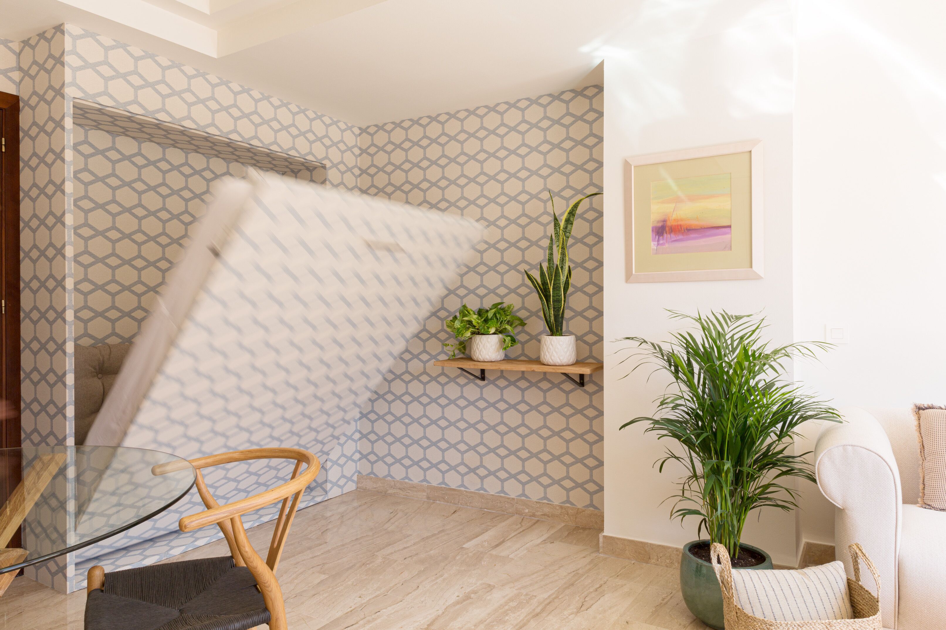 Un intérieur moderne avec un papier peint à motifs, une porte en verre, une chaise en bois, une plante en pot et un tableau encadré au mur.