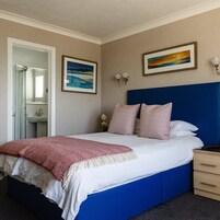 Un dormitorio con cama, mesitas de noche, un tocador, un espejo, un lavabo y dos cuadros en la pared.