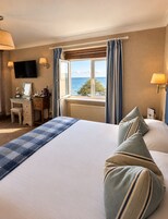 Habitación de hotel con cama, escritorio, televisión y ventana con cortinas.