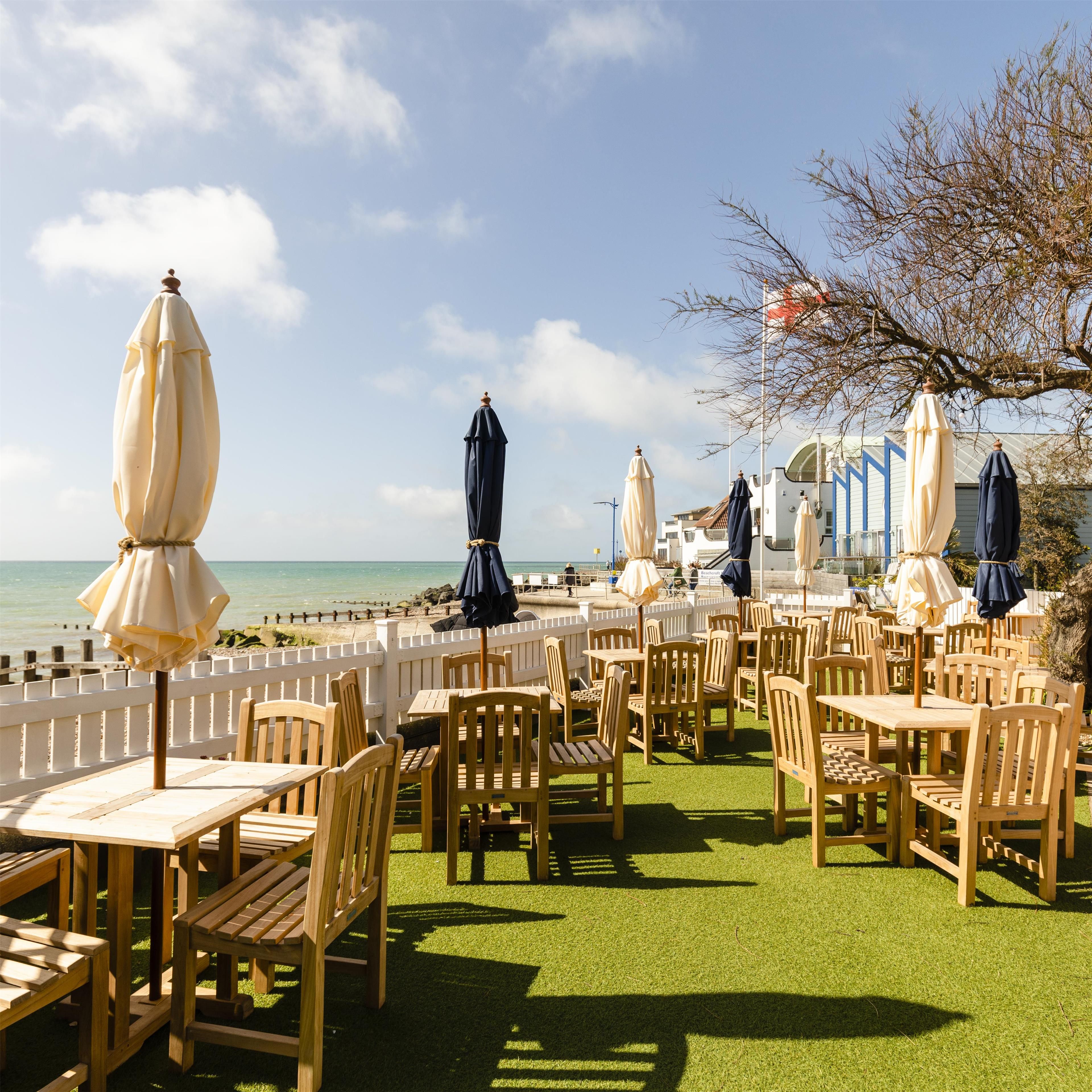A seaside restaurant with outdoor seating, a white fence, and a view of the ocean.