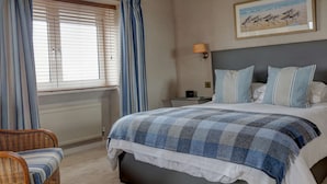 A bedroom with a bed, a nightstand, a lamp, a chair, and a painting on the wall.