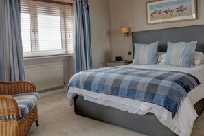 Quarto com cama, mesa de cabeceira, luminária, cadeira e um quadro na parede.