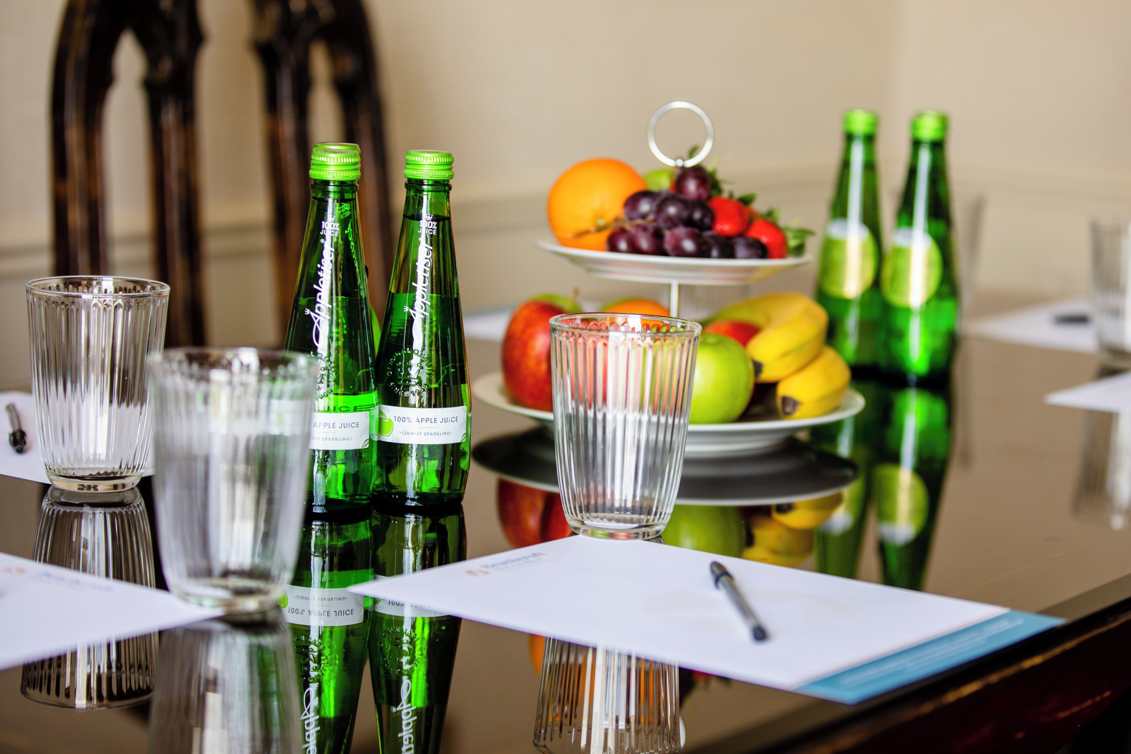 Una mesa con botellas verdes, vasos y una bandeja de frutas.