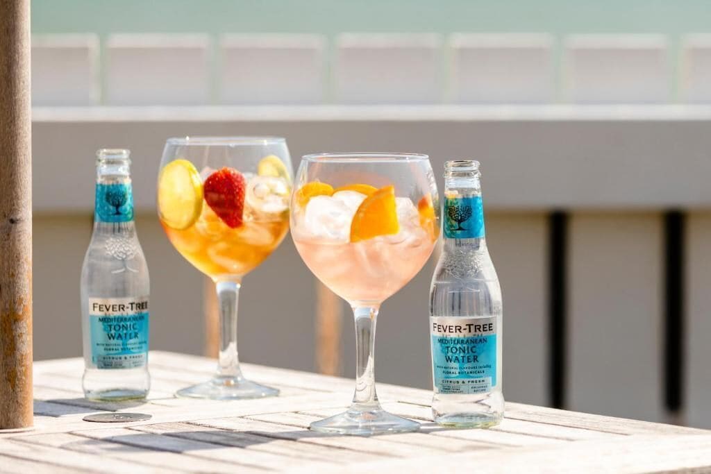 Three glasses of beverages with bottles of Fever Tree Mediterranean Tonic Water.