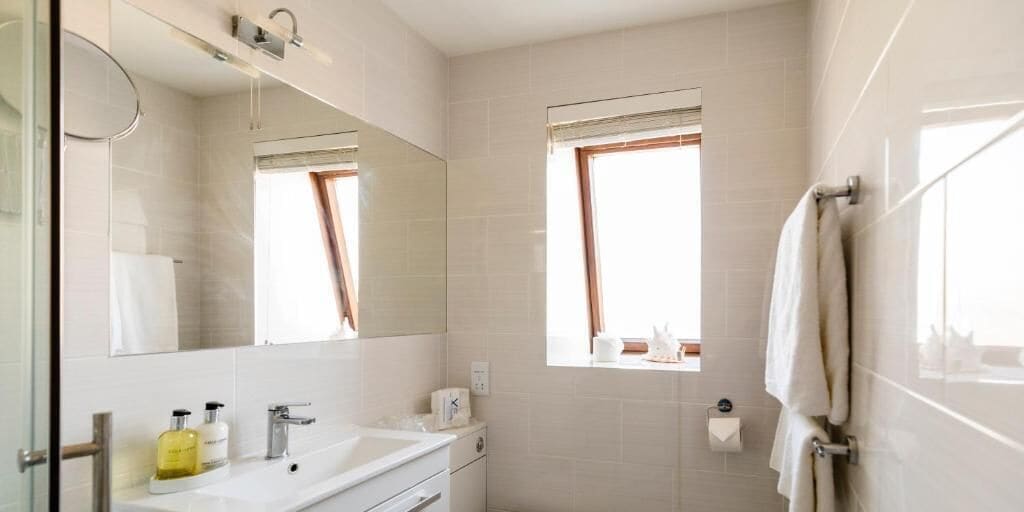 Un baño con lavamanos, espejo, ventana y toallero.