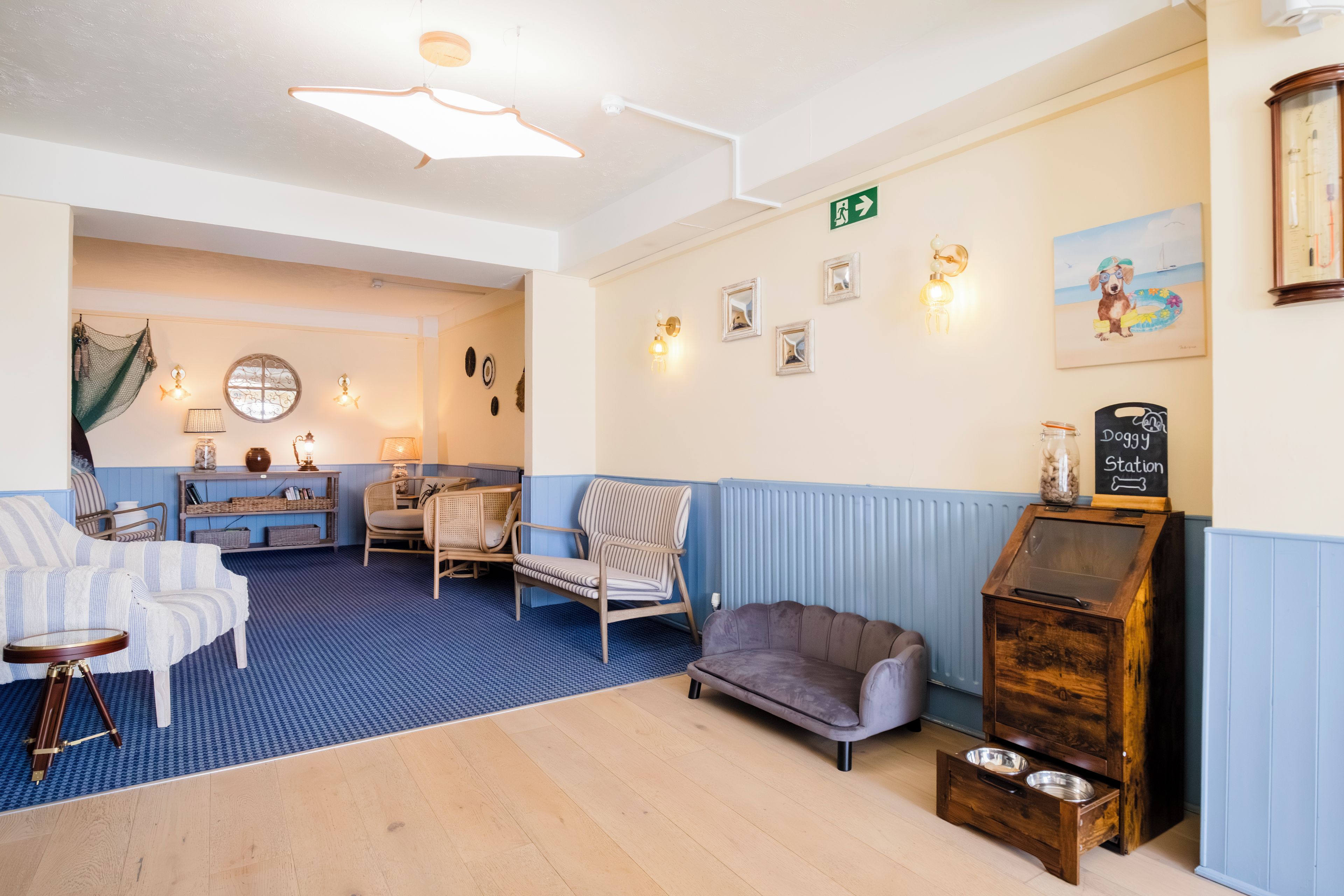 Une pièce chaleureuse aux couleurs bleu et blanc, comprenant un canapé, des fauteuils, un meuble en bois et une étagère murale agrémentée d’objets décoratifs.