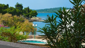 Blick über den Pool auf das klare Meer und die umliegende Grünfläche.