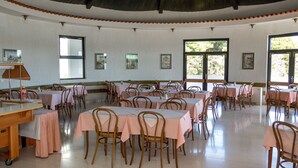 Ein geräumiger Speisesaal mit mehreren Tischen und Stühlen, großen Fenstern und einer hohen Decke.