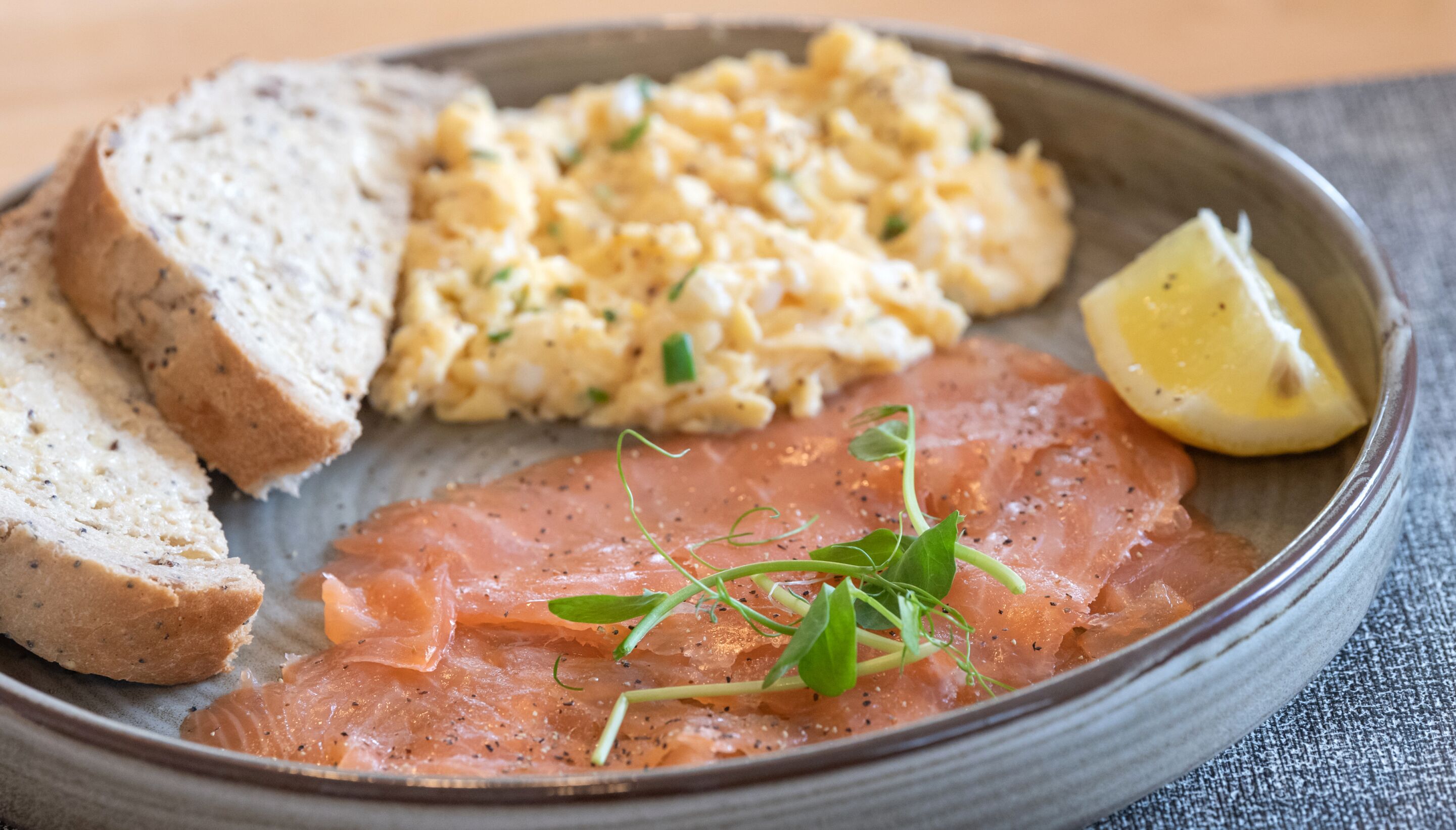 Ein Teller mit Brotscheiben, Rührei, Räucherlachs und einem Zitronenschnitz.