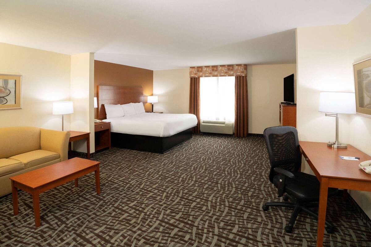 Una habitación de hotel con cama, escritorio, silla, sofá y televisor.