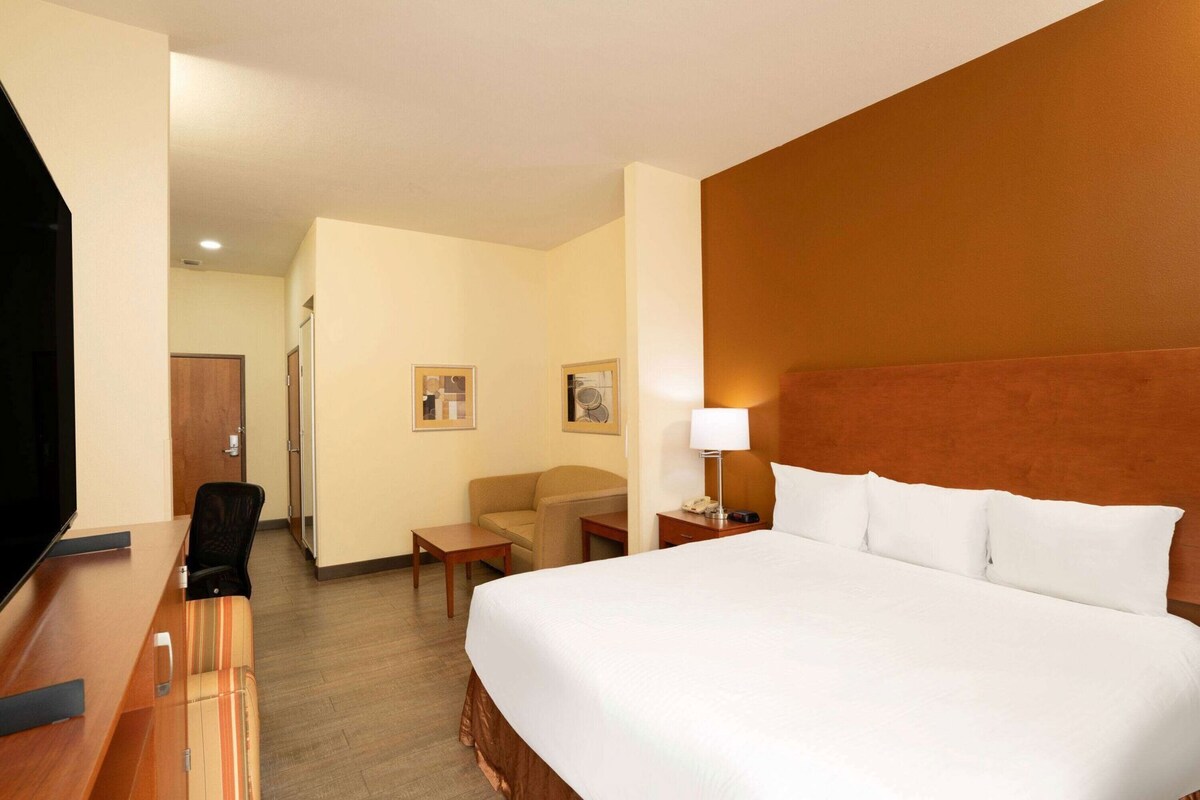Una habitación de hotel con cama, escritorio, silla, televisión y lámpara.