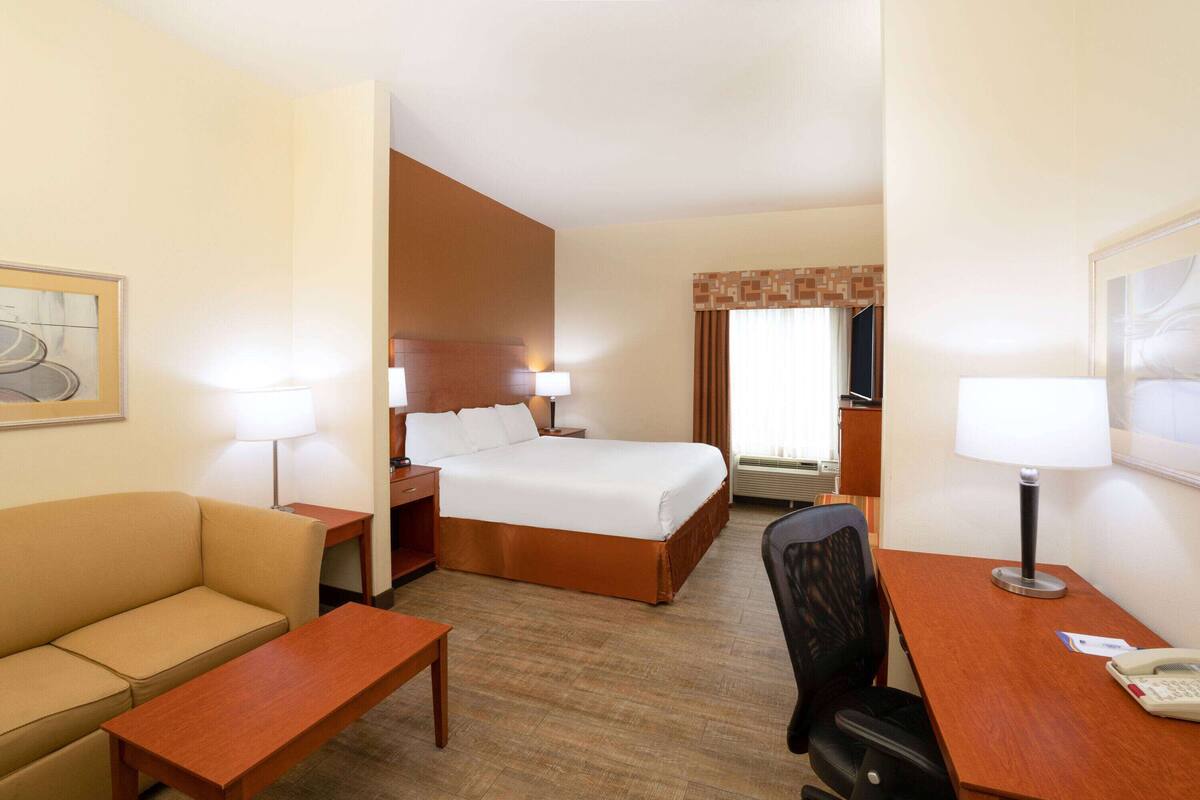Una habitación de hotel con cama, escritorio, silla, sofá y televisión.