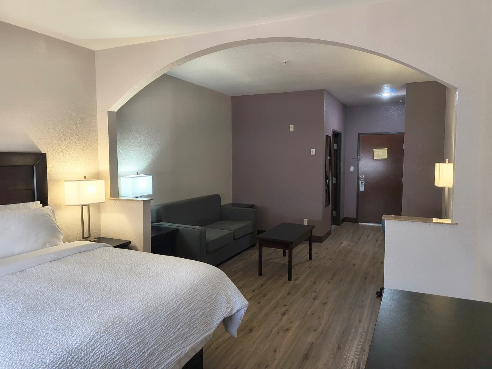 A hotel room with a bed, a sofa, a small table, and a lamp.