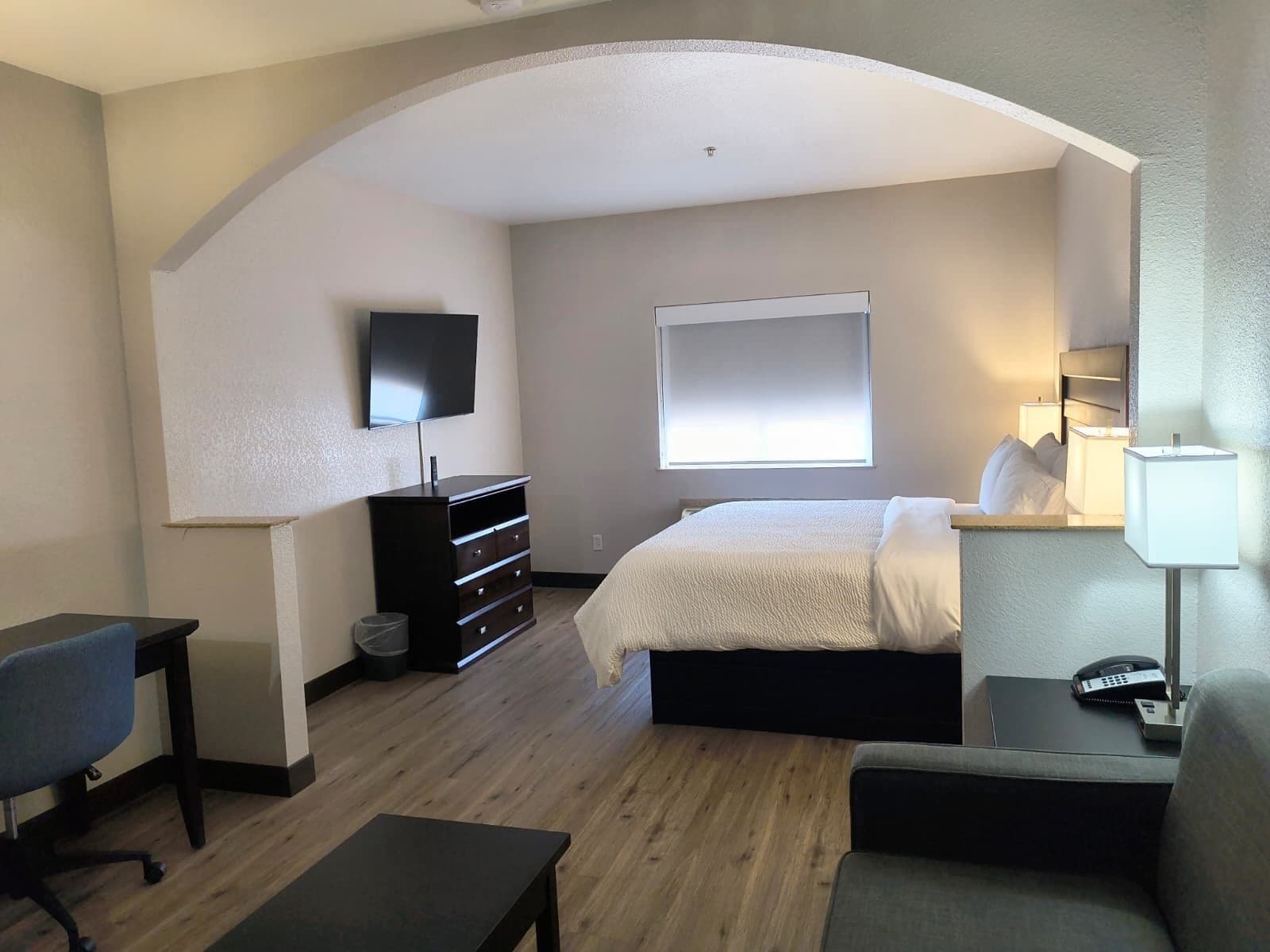 Een hotelkamer met een bed, een bureau, een stoel, een televisie, een raam en een bedlamp.