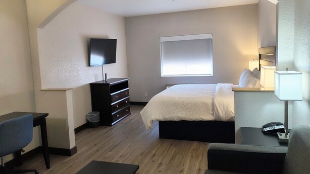 A hotel room with a bed, a desk, a chair, a TV, a window, and a bedside lamp. - Grander Inn & Suites by IHG (Tyler)