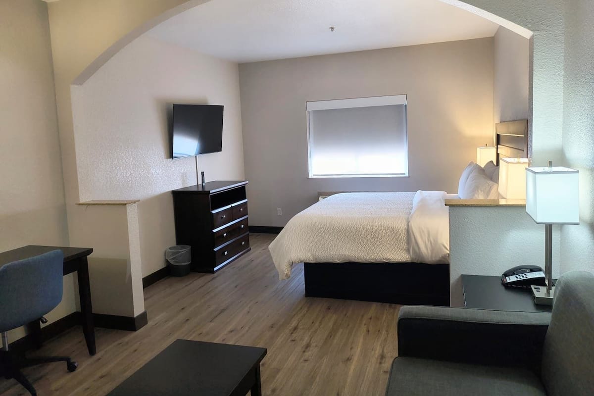 Een hotelkamer met een bed, een bureau, een stoel, een televisie, een raam en een bedlamp.