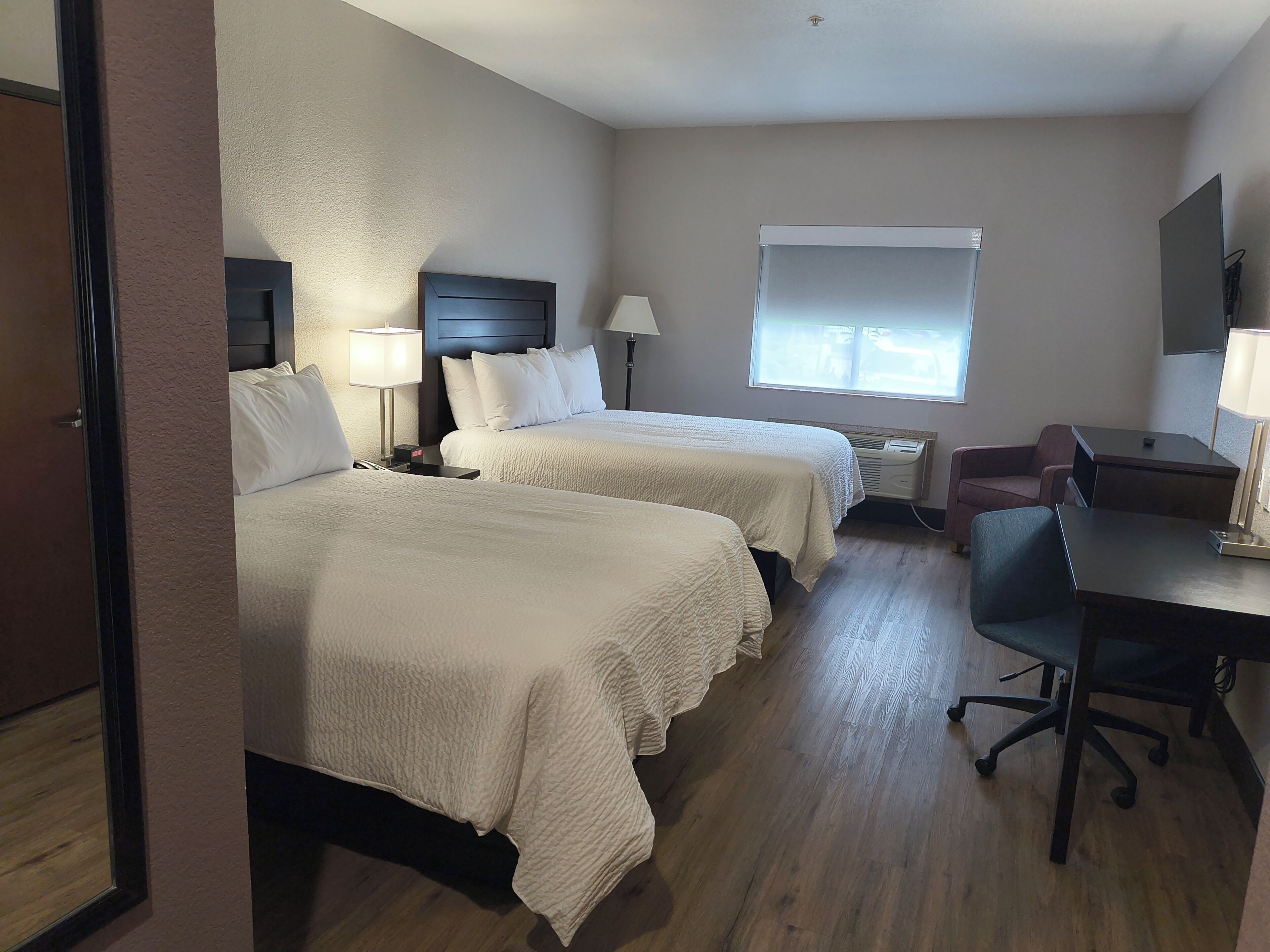 Een hotelkamer met twee bedden, een bureau, een stoel, een raam en een tv aan de muur.