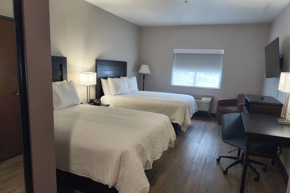 Een hotelkamer met twee bedden, een bureau, een stoel, een raam en een tv aan de muur.