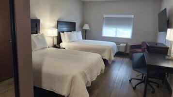 Une chambre d’hôtel avec deux lits, un bureau, une chaise, une fenêtre et un téléviseur fixé au mur.