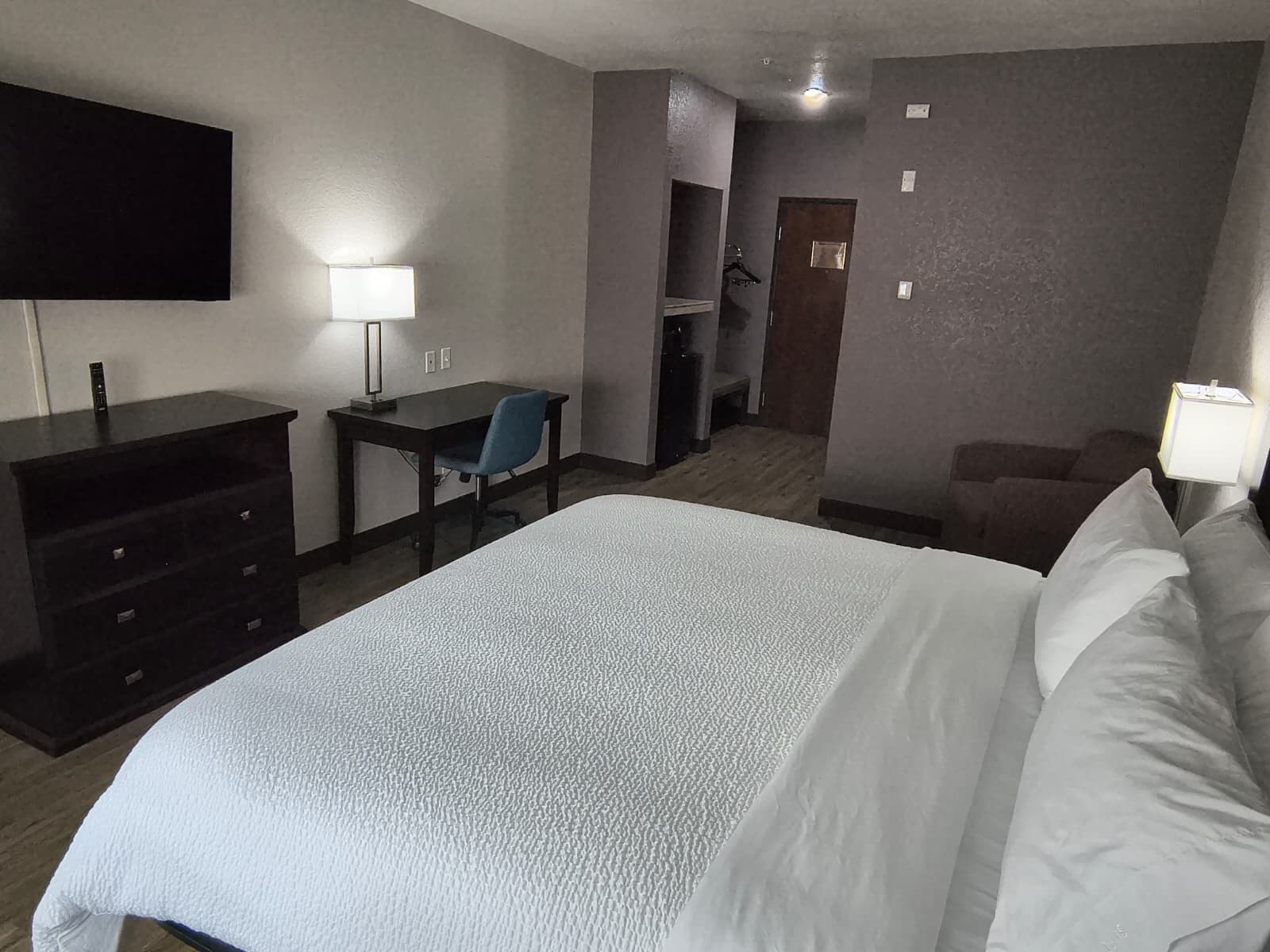Una habitación de hotel con cama, escritorio, silla, televisor y armario.