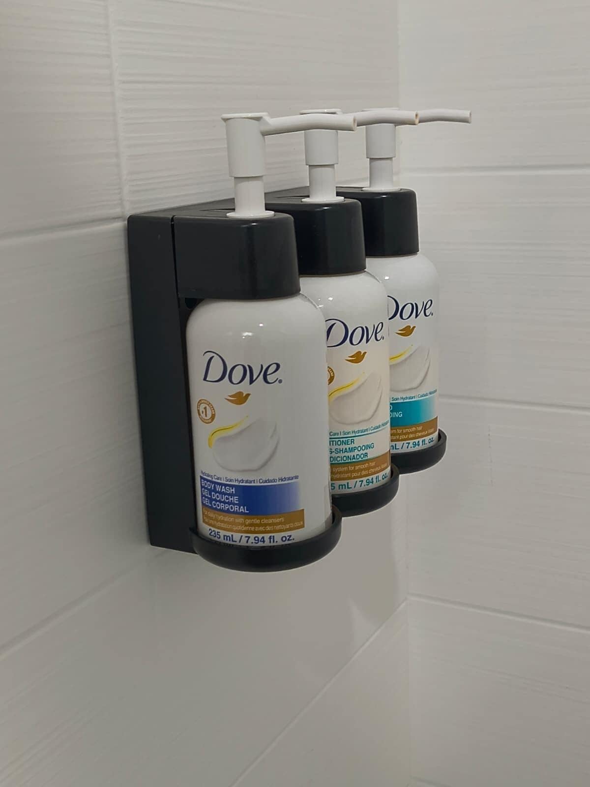 Two Dove body wash bottles mounted on a black dispenser in a bathroom.