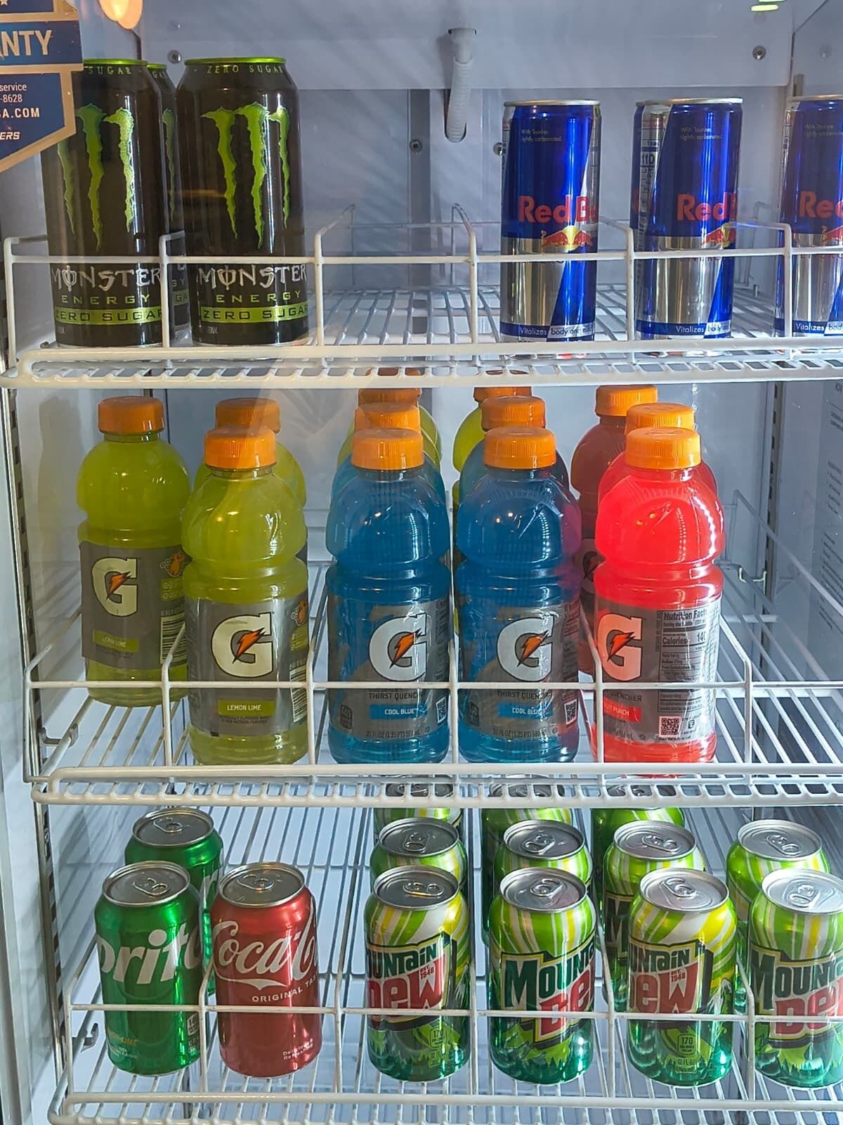 Een koelkast gevuld met verschillende drankjes, zoals Monster Energy, Red Bull, Gatorade en Mountain Dew.