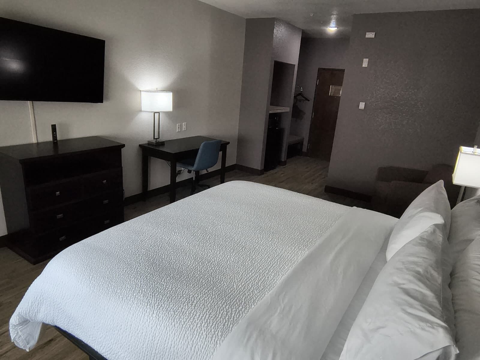 A hotel room with a large bed, a desk with a chair, a TV mounted on the wall, and a lamp.