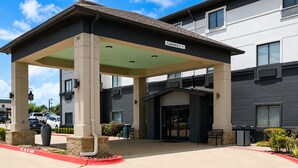 A hotel entrance with a covered waiting area, a clear sign indicating a 13' clearance, and a parking lot with a red curb. - Grander Inn & Suites by IHG (Tyler)